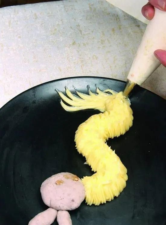 用裱花袋将自制沙拉酱裱在香芋底坯上,做出龙的造型,在龙头上点缀两颗
