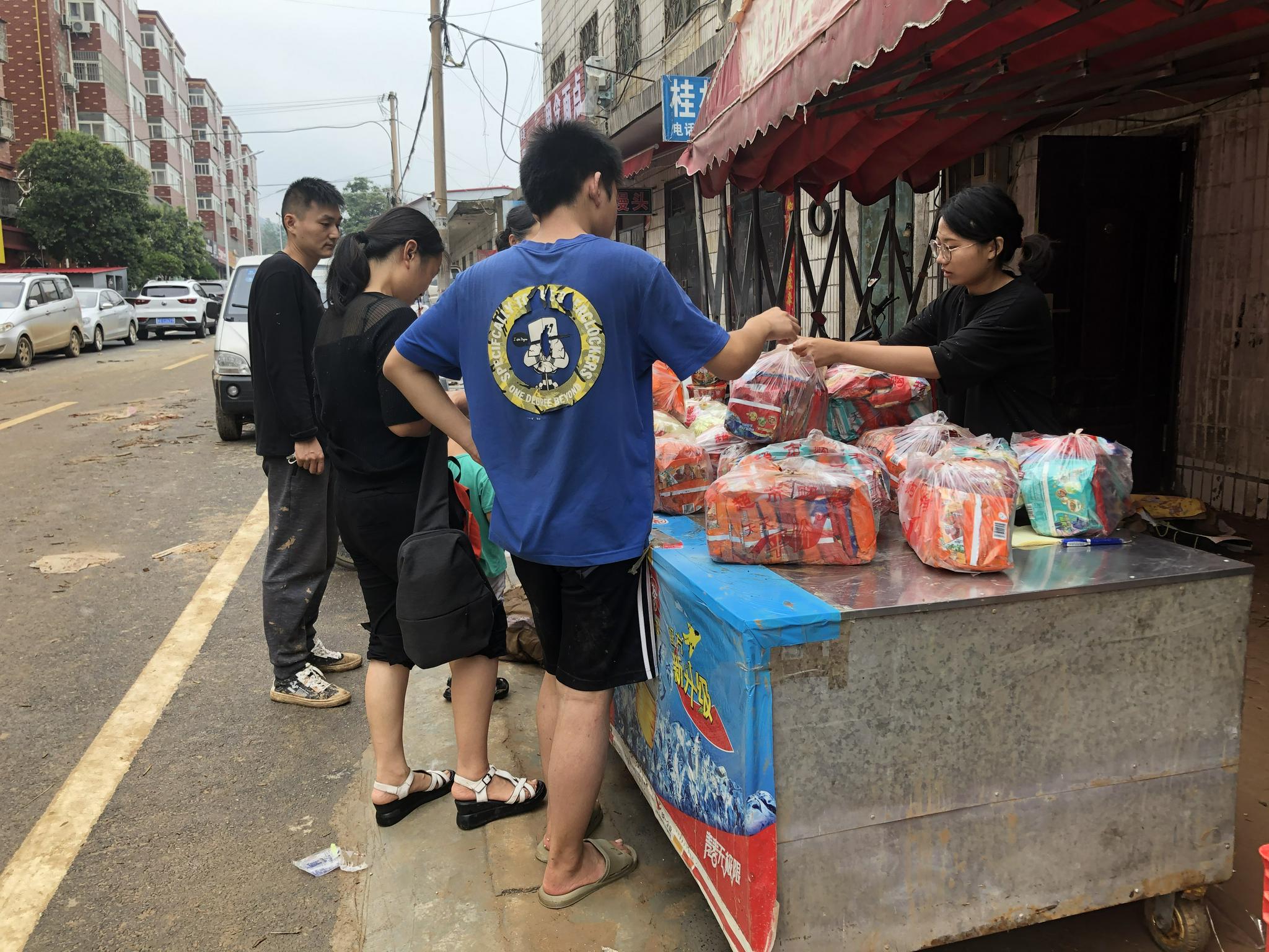 这家商店进水近一米深，许多商品被泡。图为商店主人将被水泡烂包装箱的方便面用塑料袋装起来售卖。