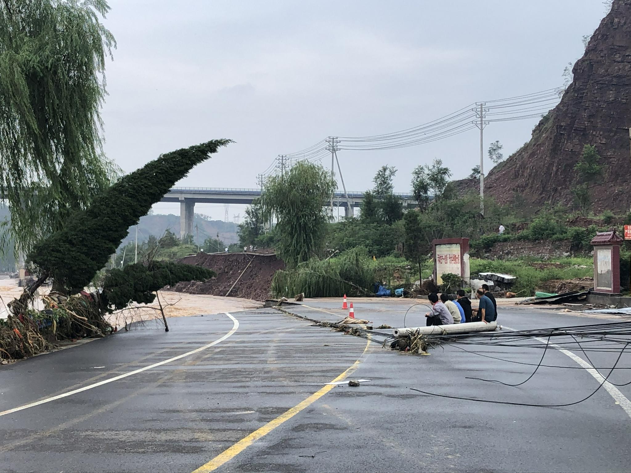 汜水河东岸的人们坐在倒掉的电线杆上看着洪水发呆。