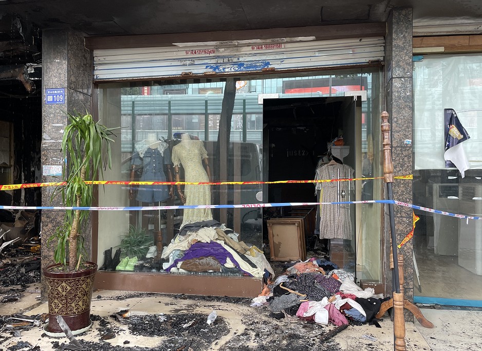 天花板的吊顶被烧得只剩下空架子但店铺内部已经被熏黑虽然服装店门口
