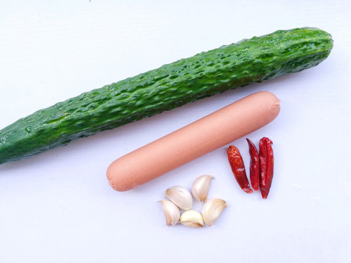 2,将黄瓜清洗干净,然后切成小块,火腿肠切成小块,大蒜切成片,干辣椒