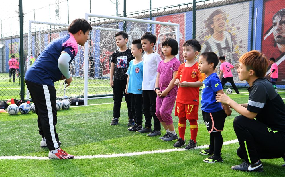 少儿足球启蒙班的教练（左一）向小学员讲解动作要领。