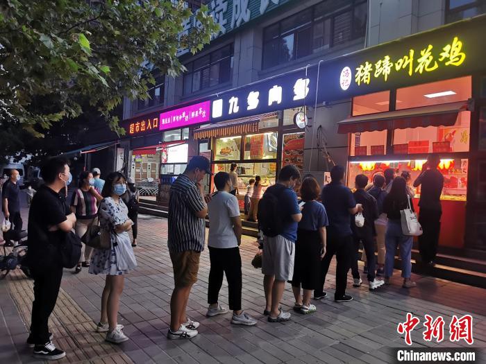 图为8月27日晚间，郑州市民排队购买小吃，城市烟火气息渐回。韩章云 摄