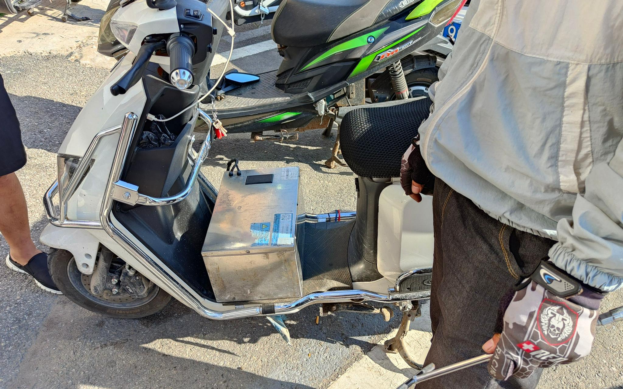  8月20日，十里河附近的哈啰电动车门口，一名骑手的改装电动车脚踏板位置放着外接电池。  新京报记者刘瑞明 摄