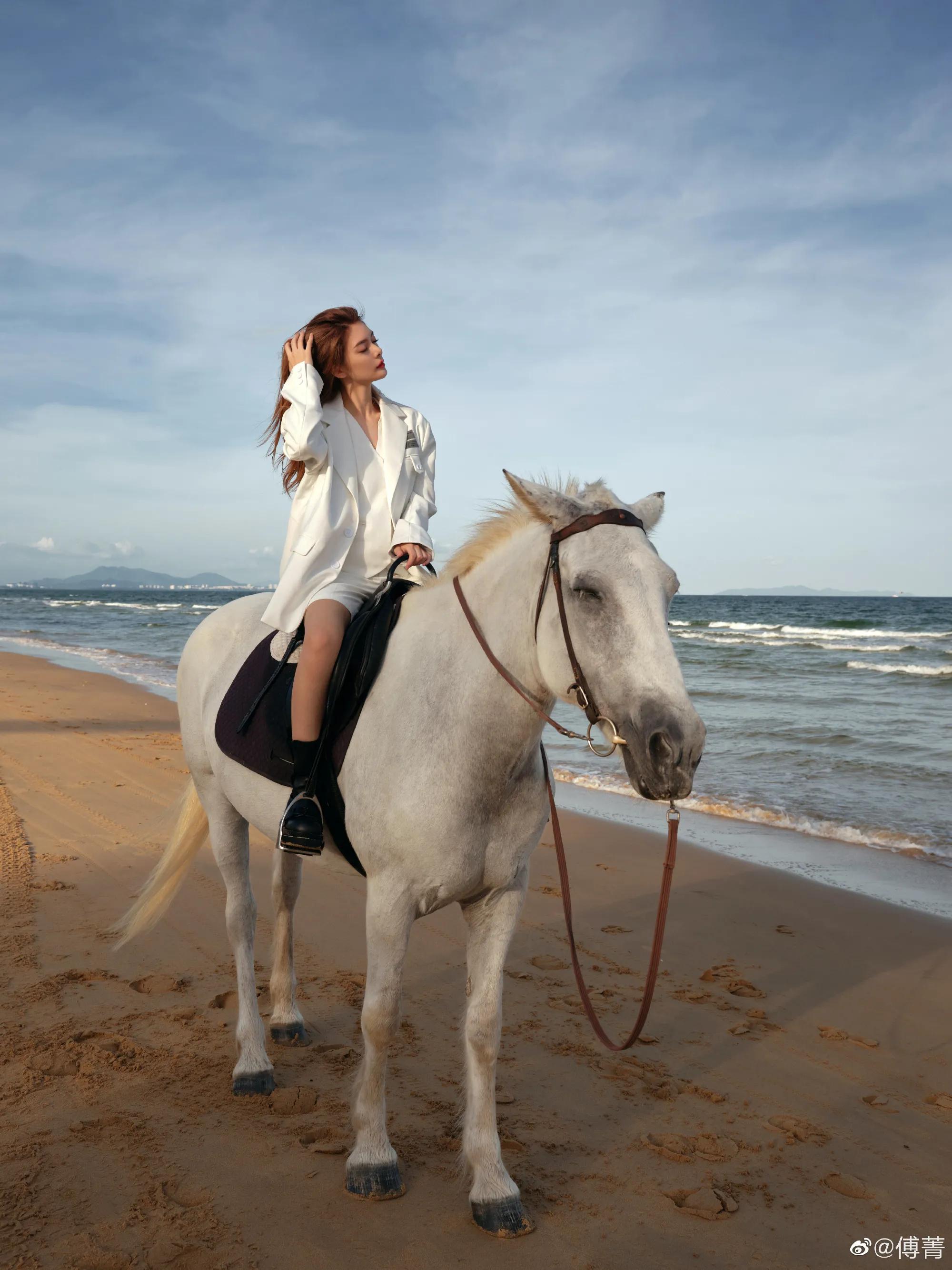 傅菁身穿白色刺绣西装,身骑白马的海边酷飒女孩__财经头条