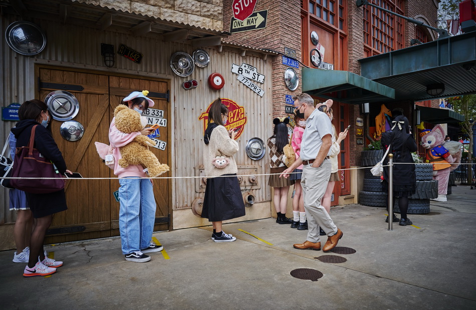 迪士尼乐园工作人员提醒排队游客保持安全社交距离。