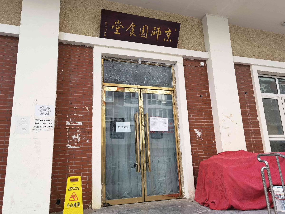 紧锁的大门上方挂着一块写着"京师园食堂"的牌匾,门上还贴着一张落款
