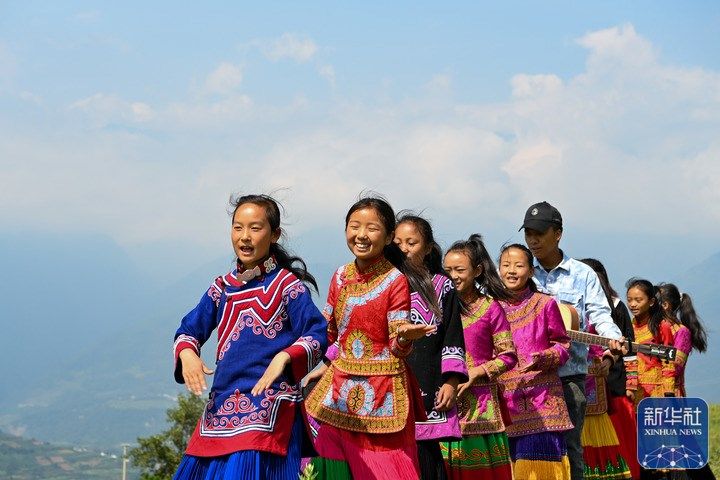 △8月6日,在四川省凉山彝族自治州普格县大槽乡,妞妞们和吉布小龙在户外唱歌。在彝族家庭里,父母一般把女儿唤作“妞妞”。在位于四川省凉山彝族自治州普格县的大槽乡中心小学,有一个全是由妞妞组成的童声合唱团——妞妞合唱团。2018年的一个课间,老师吉布小龙抱着吉他坐在操场边轻声弹唱。几个女孩循着歌声围坐了过来,跟着音乐一起小声哼唱。“你们想唱歌吗?”吉布小龙问到。女孩们没有说话,眨着眼睛,怯生生地点点头。在小龙老师的鼓励下,音乐教室里的妞妞渐渐多了起来。通过在抖音等短视频平台上的创作分享,吉布小龙让更多人看到了妞妞合唱团。2021年夏天,妞妞合唱团接到邀请,去北京参加了音乐节。妞妞们唱着歌走出大山,走向更大的舞台。