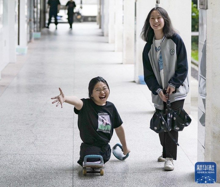 △5月10日,蒋张子怡(左)和同学在学校的走廊聊天。16岁的蒋张子怡是江西上饶中学高中一年级的学生。2010年一场车祸夺去了她的双腿,如今的她只能依靠滑板代步,用双手前行,为此,大伙都称她“滑板姑娘”。身体虽然残疾了,但却没有磨灭蒋张子怡对美好生活的信念和渴望。除了每天由母亲张水香骑着电动车接送她上学读书外,她还有着广泛的兴趣爱好,喜爱舞蹈、播音主持和写作,希望可以成为一个多才多艺的人。