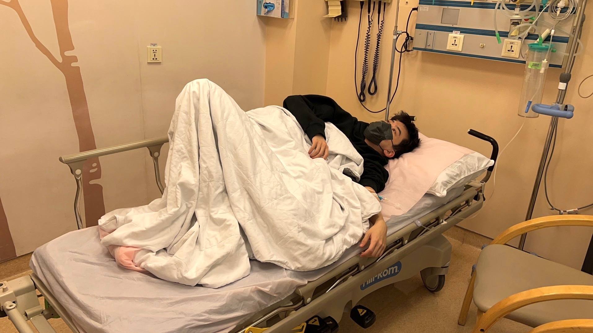 费启鸣躺在病床上,双腿弯曲,整个人看起来都比较软弱无力,其中一只手