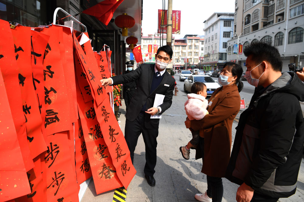 韦寒贵一家被大化瑶族自治县县城一家银行门前摆放的对联所吸引（2月3日摄）。新华社记者 周华 摄