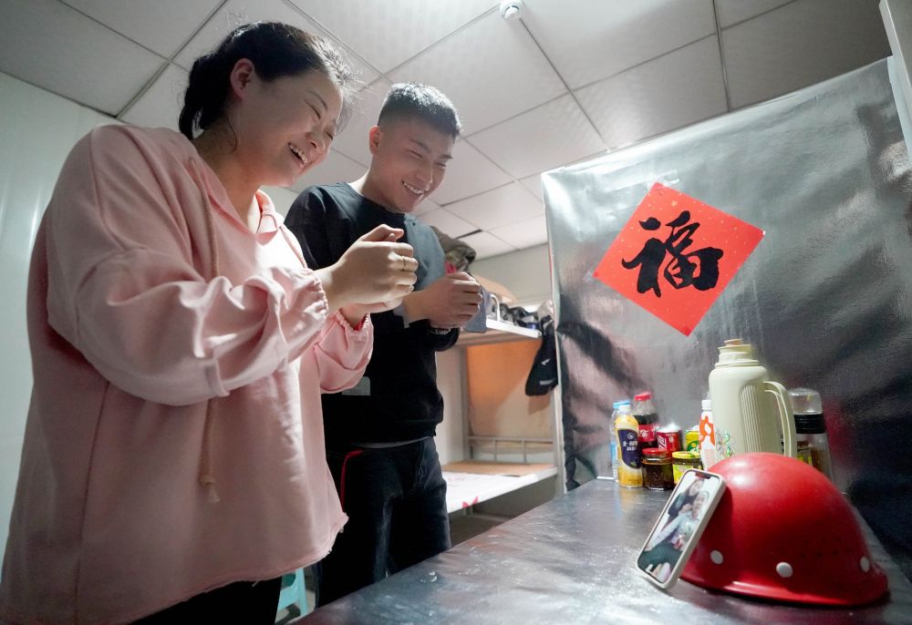 ↑2月11日，来自吉林长春的北京丰台火车站改扩建工程施工管理人员杜岩、王一竹（左）夫妇在宿舍内通过手机视频给王一竹父母拜年。新华社记者 王毓国 摄