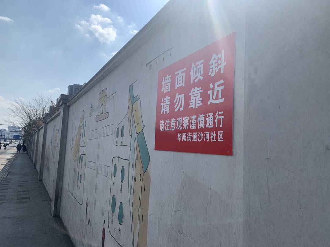 有华阳街道沙河社区张贴的红色的警示牌,上面写着"墙面倾斜,请勿靠近