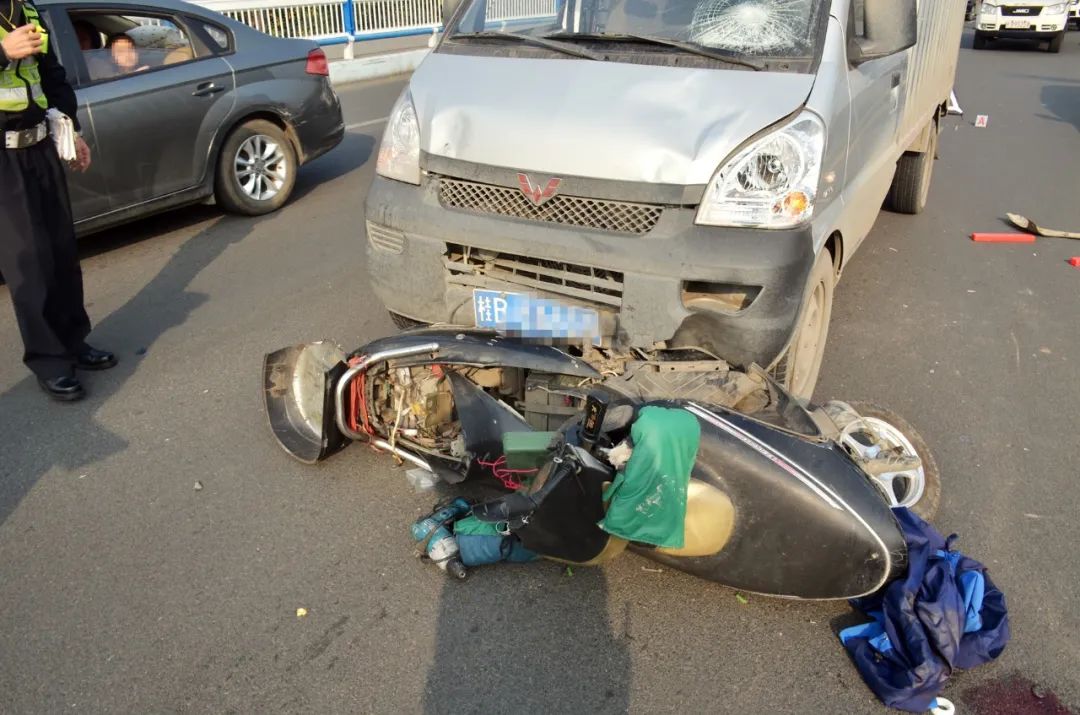 电动车被压在小货车车头下,车身严重损坏,车零件以及私人物件散落满地