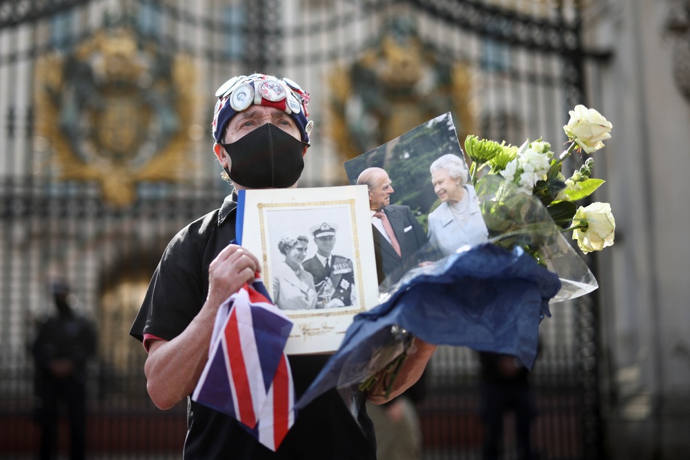 当地时间2021年4月9日，一位伦敦市民在白金汉宫门前准备摆放鲜花。