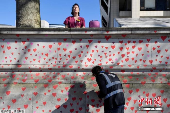 资料图：当地时间3月29日，英国伦敦，志愿者和新冠疫情死难者家属在墙上绘制爱心图案，悼念新冠疫情死难者。