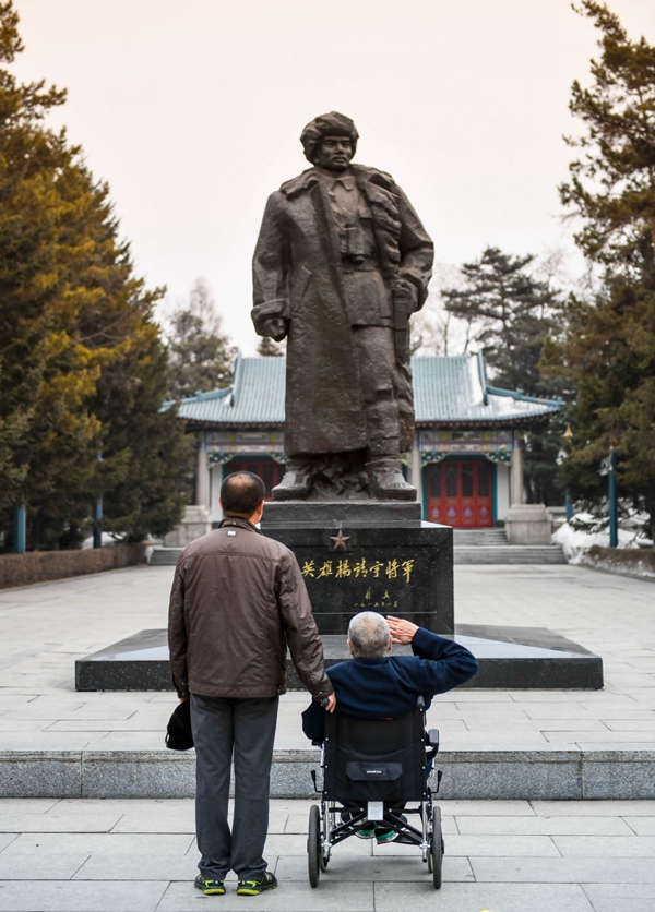 ↑多次立下军功的英雄老兵徐振明（坐轮椅者），60多年如一日守护着杨靖宇烈士陵园，他的儿子也在陵园工作，至今守陵已有40年。这是父子二人在吉林省通化市杨靖宇烈士陵园向杨靖宇将军戎装铜像致敬（2017年3月17日摄）。新华社记者 王昊飞 摄