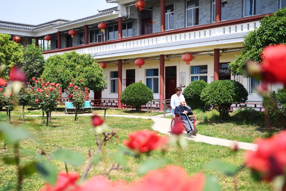 △2021年5月2日,在河南驻马店市经济开发区重度残疾人集中托养中心,护工推着入住人员从院子里走过。