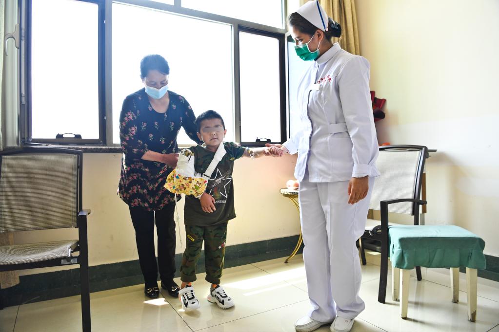 在新疆医科大学附属中医医院，断臂男孩在妈妈苏迪乌麦·伊敏托合提（左）和医护人员搀扶下活动（5月9日摄）。新华社发（汤永 摄）