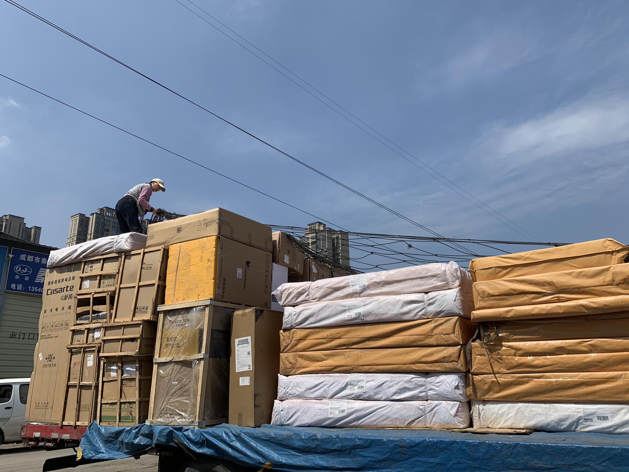在赶往另一个卸货点之前，谢琳爬上卡车，用网绳勒紧货物。高佳摄