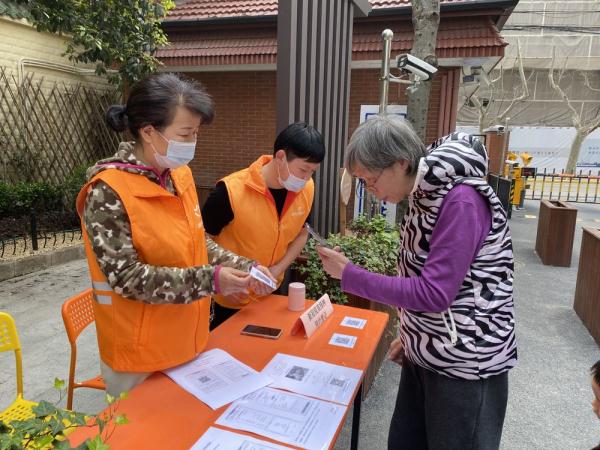 徐汇区天平街道宛平居委会工作人员在小区内设立登记点，向居民介绍相关新冠疫苗的接种事宜，并帮助有需要的老年人在线预约（受访单位供图）