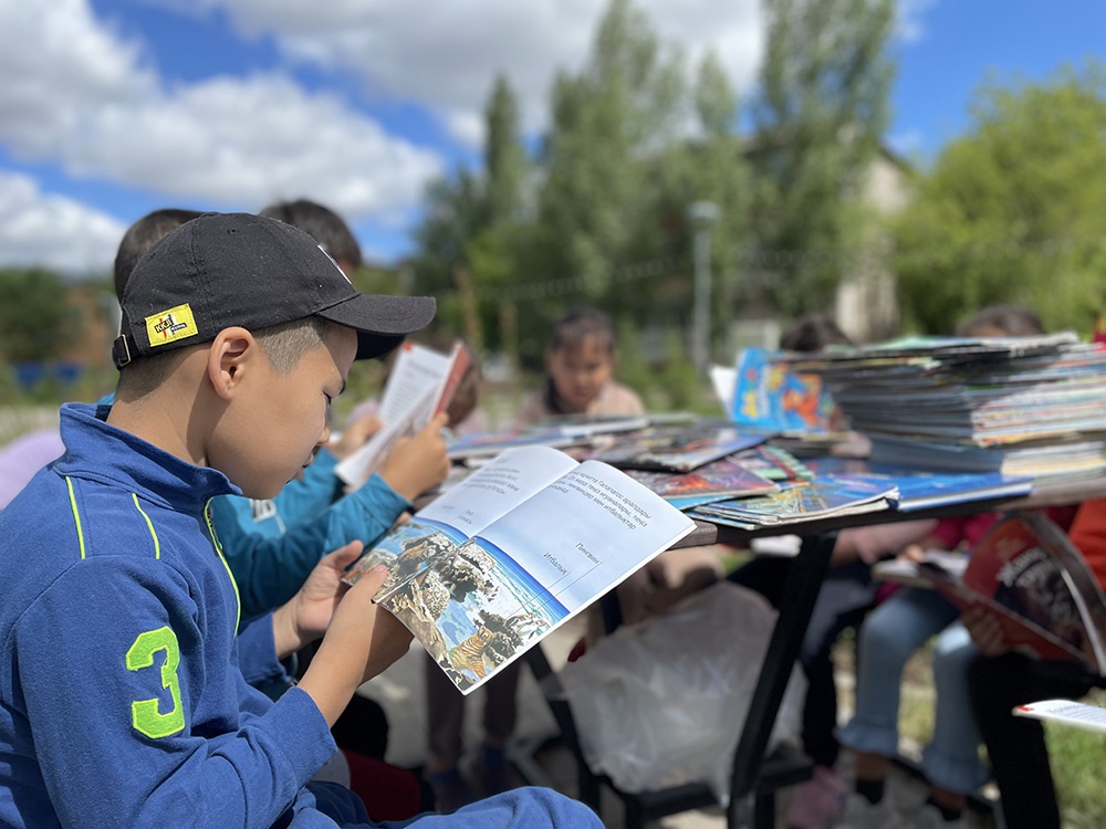 当地时间2021年6月19日，哈萨克斯坦首都努尔苏丹，随着疫情形势逐渐改善，当地迎来了一场小型“露天图书馆”阅读活动。图为参加活动的民众围绕在临时搭建的简易书柜前阅览图书。