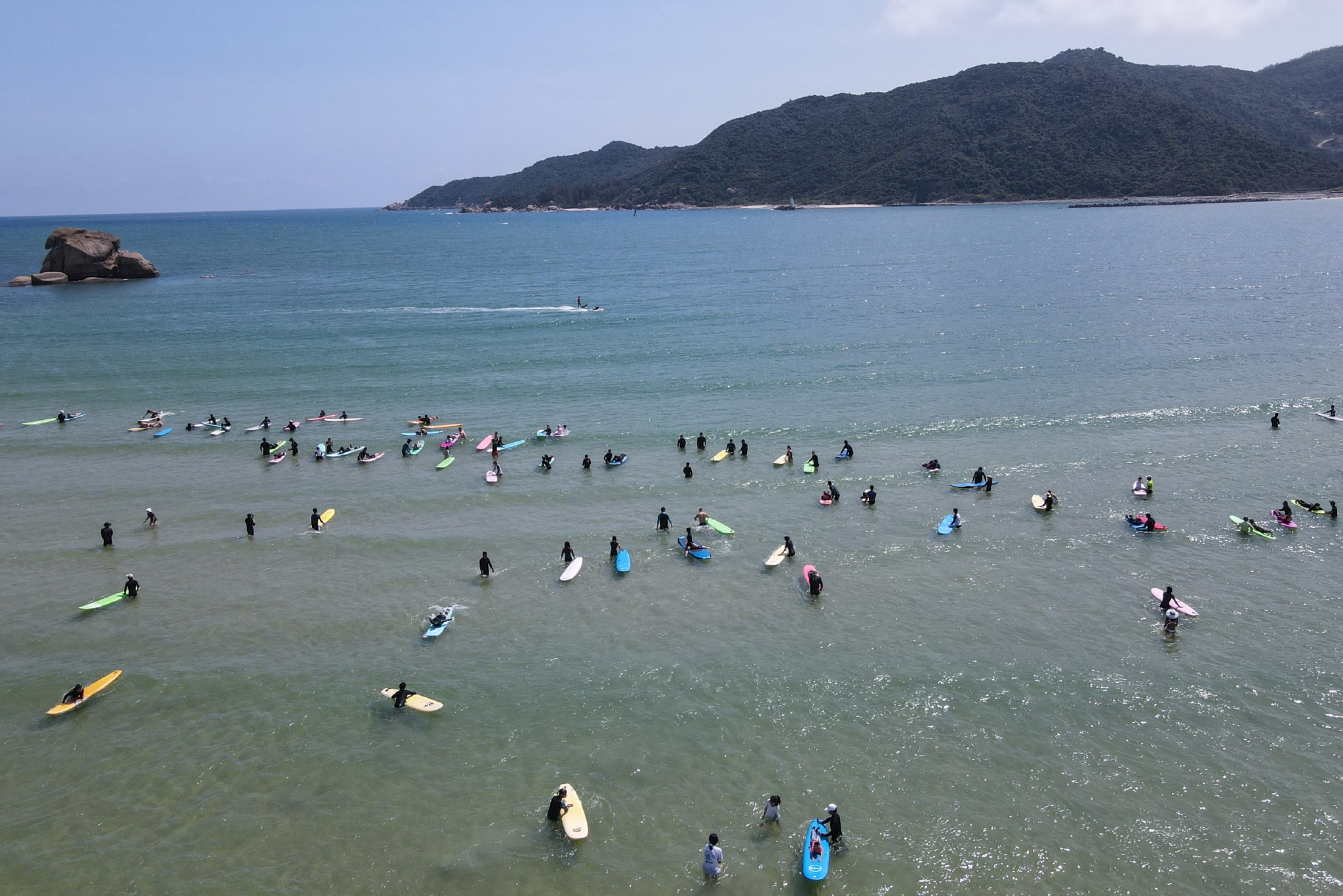 2月13日,游客在海南三亚皇后湾海域体验冲浪运动(无人机照片).