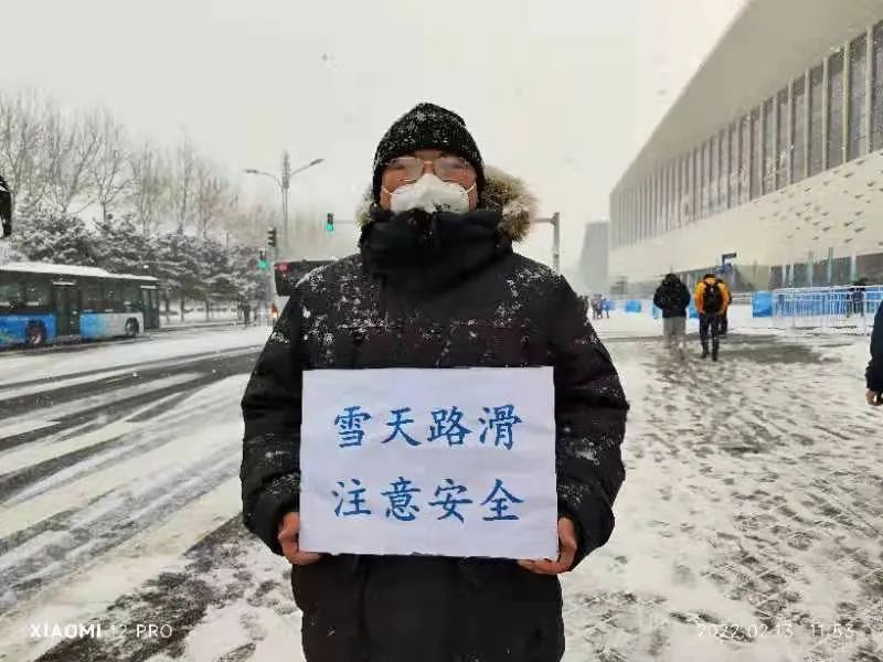 北京冬奥会主媒体中心门口工作人员手持安全提示牌站立雪中纹丝帛动