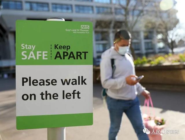 3月27日，在英国伦敦一家医院，一名佩戴口罩的男子走过告示牌。新华社发
