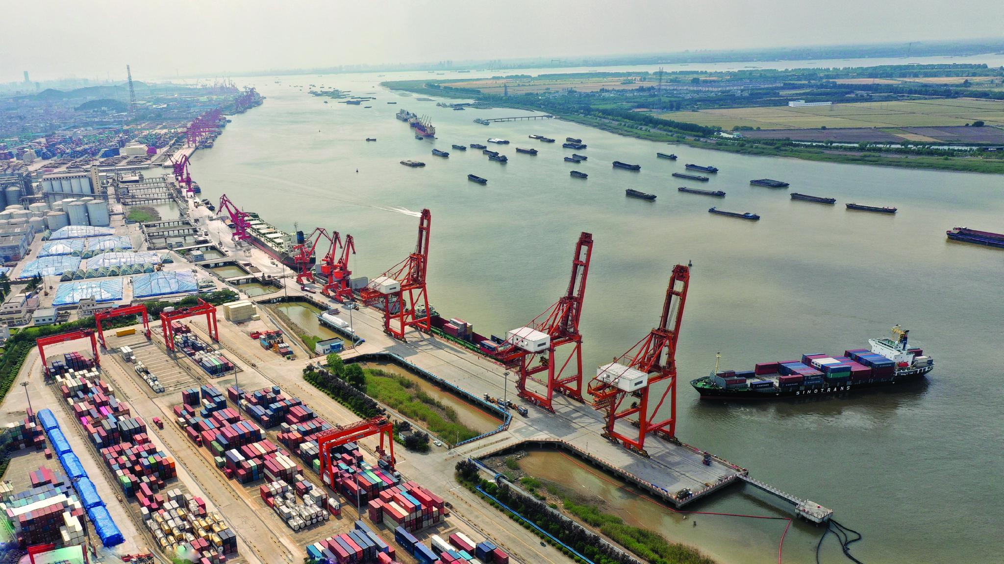 钢材,木材等生产生活物资的船舶在长江江苏省张家港段有序航行,码头上