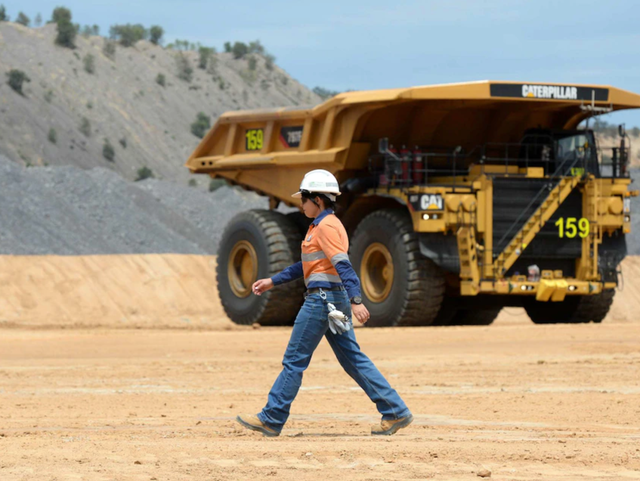 西澳州一处矿山，戴着安全帽的女员工从采矿卡车前走过（图自澳大利亚广播公司）