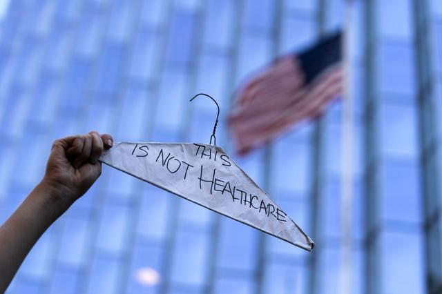 6月24日，在美国洛杉矶，堕胎权支持者手举挂着标语的衣架进行抗议。新华社 图