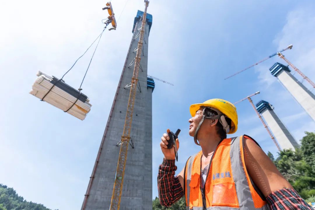 的渝湘复线高速公路芦沟河特大桥建设现场,工人正在指挥塔吊运输材料