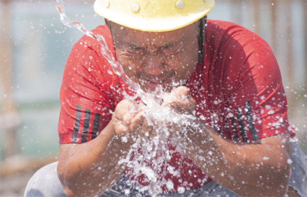 7月15日，在湖南省永州市道县中医医院整体搬迁建设项目工地，建设者在工作间隙冲水解暑。新华社 图