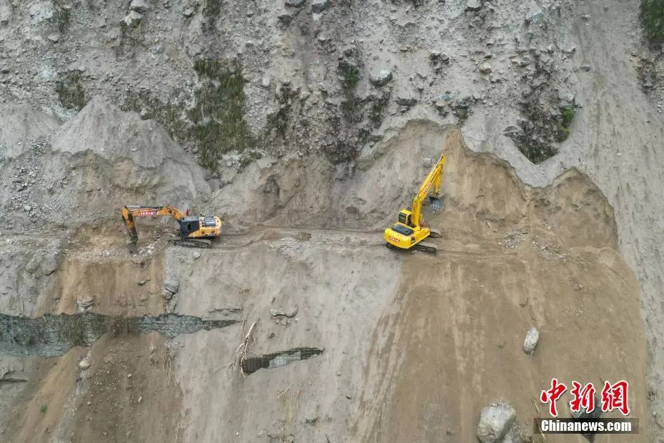 9月9日，四川泸定，抢险人员驾驶挖掘机在陡壁上抢修磨西镇赶赴海螺沟景区的蹊径。张浪 摄