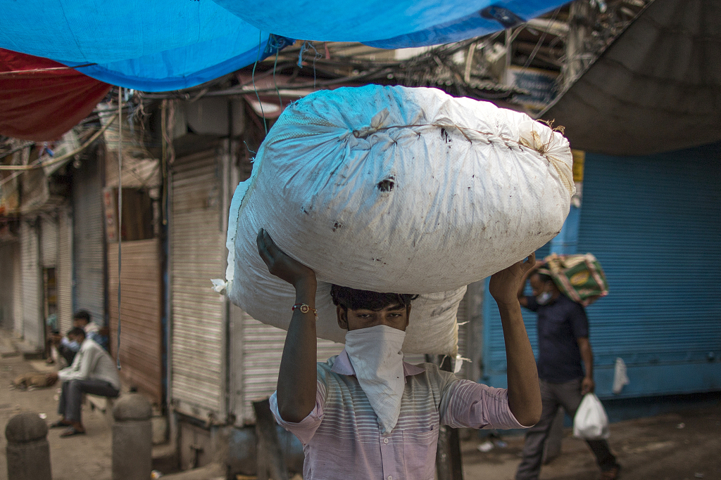当地时期2020年8月31日，印度新德里，戴着口罩的搬运领班上顶着一个袋子。人民视觉 尊府图
