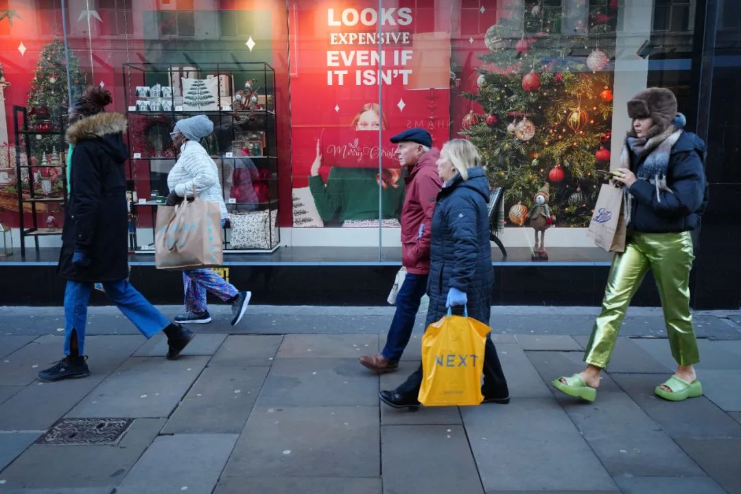 ▲当地时间2022年12月13日，人们走过英国曼彻斯特街上的促销广告。居高不下的通胀之下，英国圣诞购物季遭遇逆风，约六成受访者表示会减少圣诞节支出。图/新华社