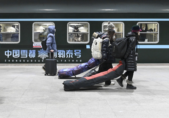 12月28日，在乌鲁木齐站，旅客从Y965次“中国雪都·阿勒泰号”冰雪游旅客列车旁走过。（新华社记者 郝建伟 摄）