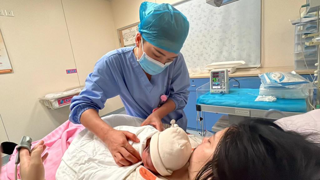 助产士陈燕婷把新生儿宽宽放到母亲林小梅身上进行早接触.