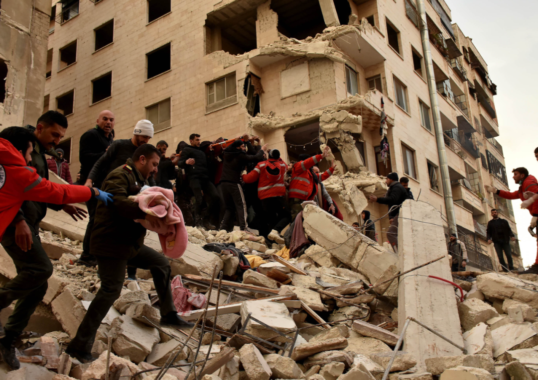 2月6日，人们在叙利亚哈马省一处倒塌的建筑上进行救援。新华社发