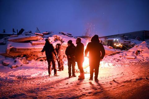2月7日晚，在土耳其卡赫拉曼马拉什省南部的埃尔比斯坦地区，救援人员在废墟旁烧火取暖。新华社记者沙达提摄