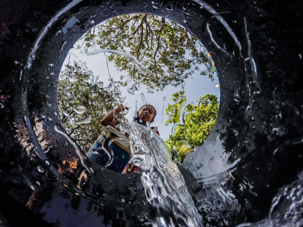 　3月22日，在菲律宾奎松市的一处水井附近，居民将水倒入桶里。新华社发（乌马利摄）