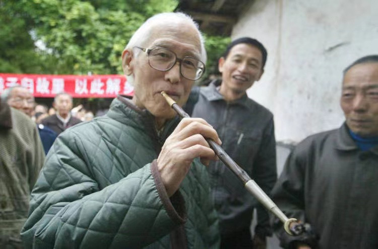 △2005年10月23日，余光中回到魂牵梦萦60载的“江北悦来场”，在现场他还抽起了老式旱烟。资料图片