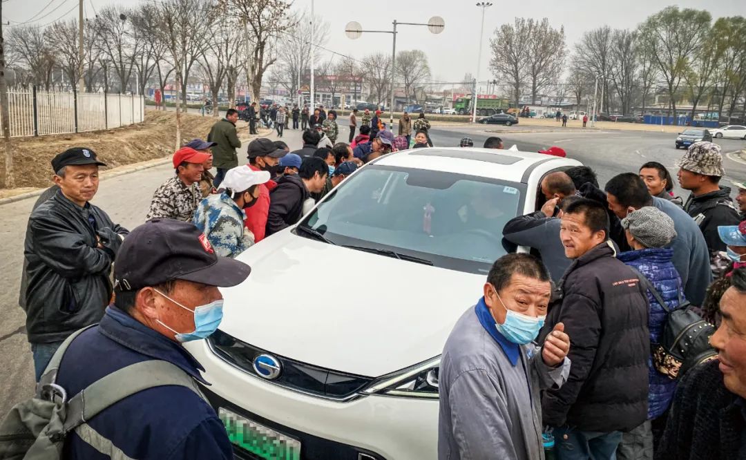 有人驾车前来招工地小工,工人们迅速围上去争相推销自己。