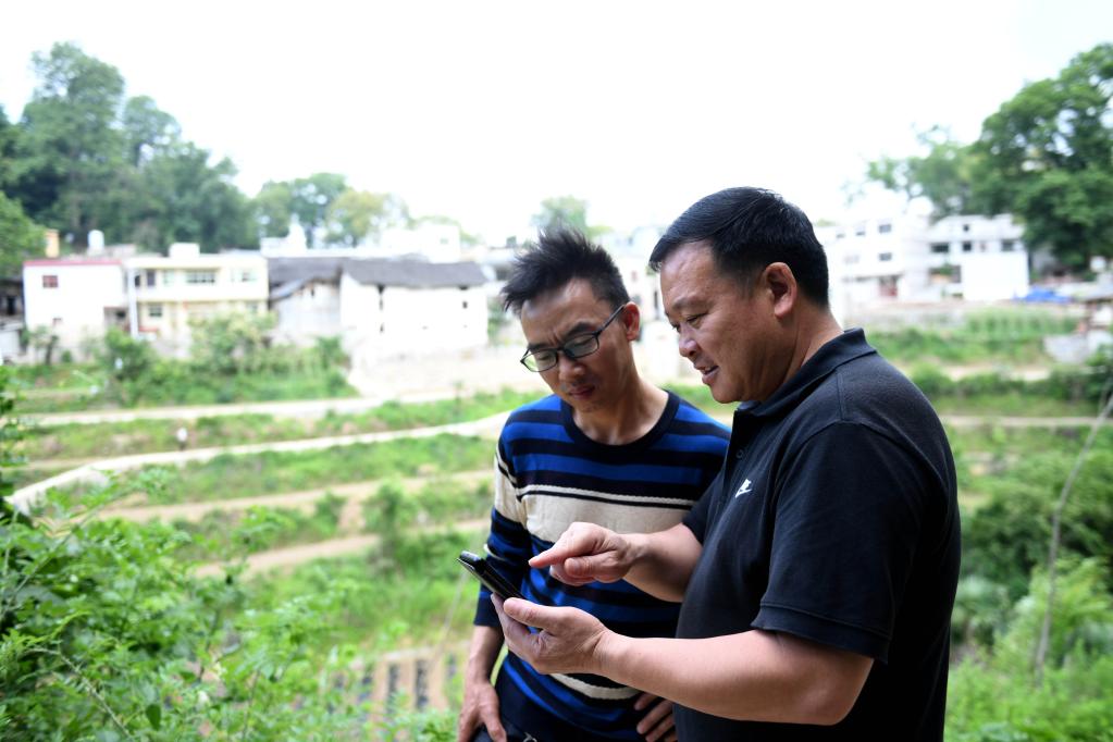 龙里县醒狮镇大岩村党支部副书记韦吉良(右一)指导村民使用"黔村规"