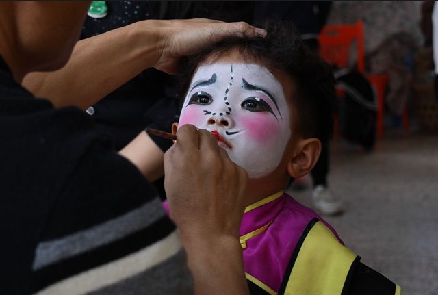 普宁南山英歌队演出前,化妆师宋才正在为"小时迁"陈楷铭上妆.
