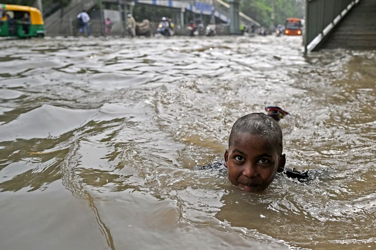 7月14日,印度新德里,一名儿童在被洪水淹没的街道上游泳.