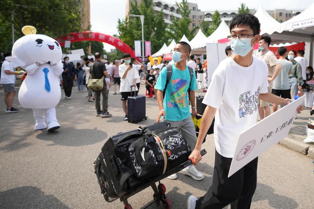 在某大学迎新点,一位学生(右)举着院系牌子帮助新生运送行李.