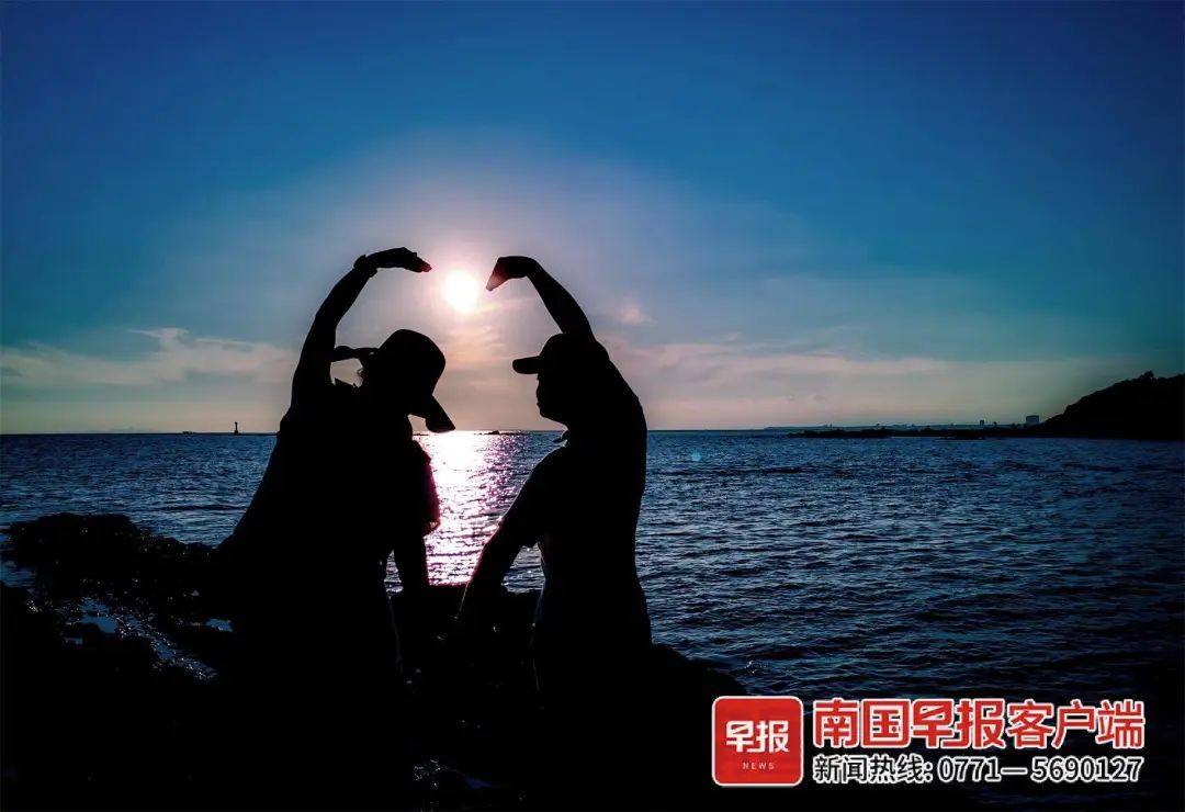 在防城港市的怪石滩,一对情侣对着落日比出爱心形状.