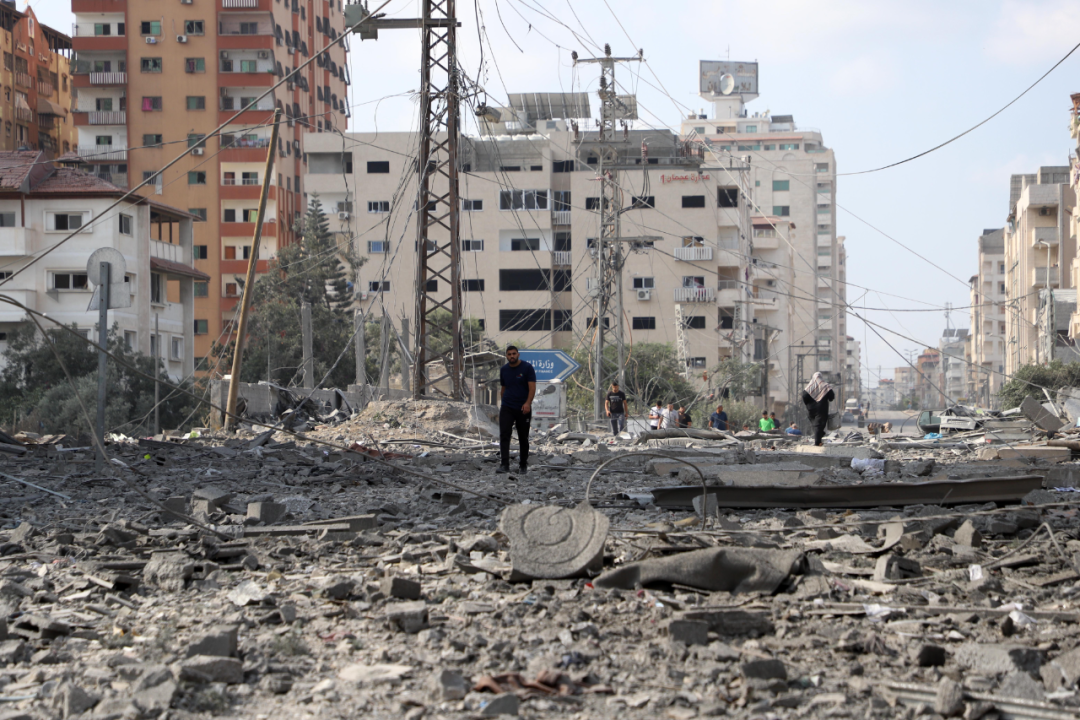 10月10日，在加沙城，人们走过被以色列空袭炸毁的建筑废墟。新华社发（里泽克·阿卜杜勒贾瓦德摄）